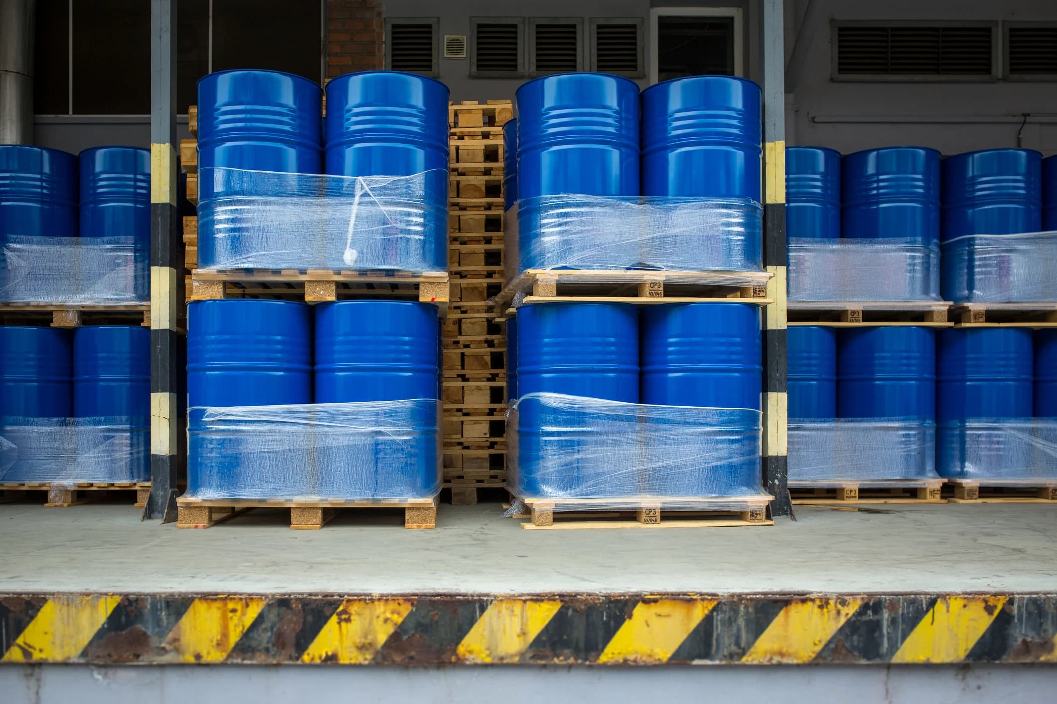 Blue steel drums stacked and shrink-wrapped on pallets at a loading dock