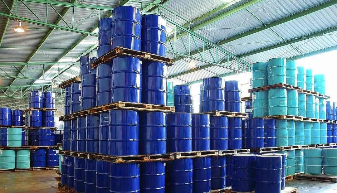 Blue and teal steel drums stacked high in a warehouse